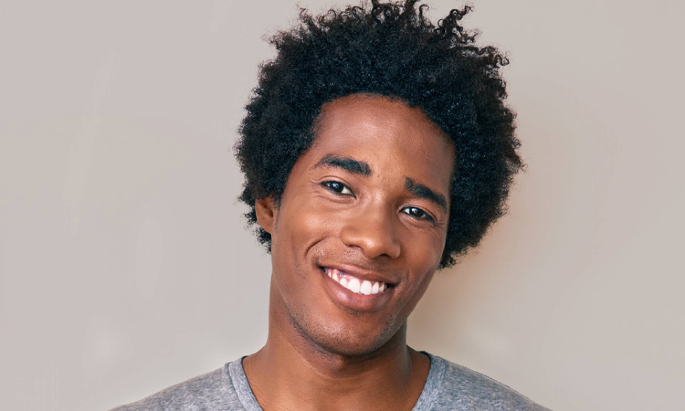 Friendly, good-looking, smiling African American man leaning against a wall with a full head of afro hair and a good hairline