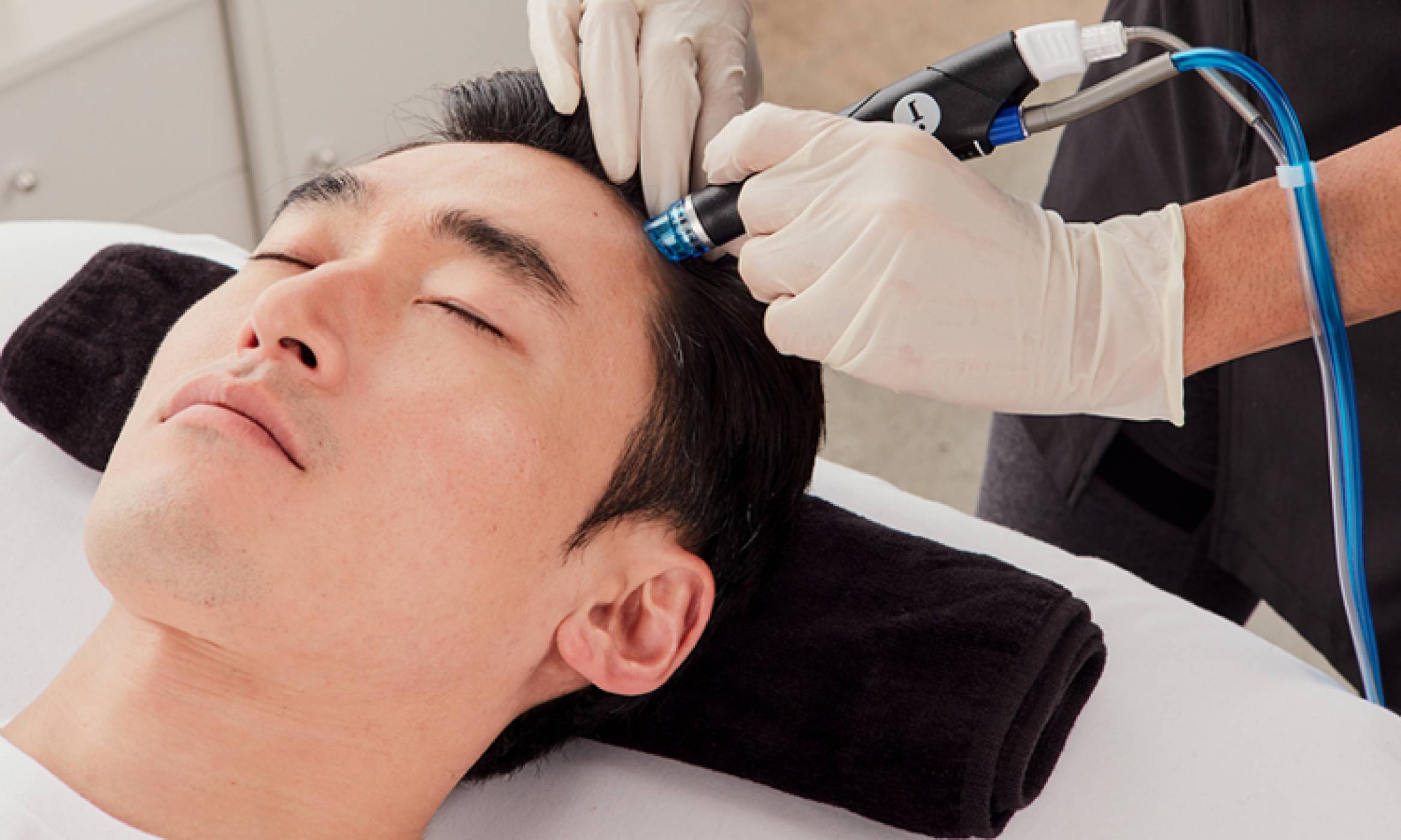 Close-up of relaxed man with eyes closed undergoing HydraFacial Keravive treatment for hair loss to help regrow thicker hair.