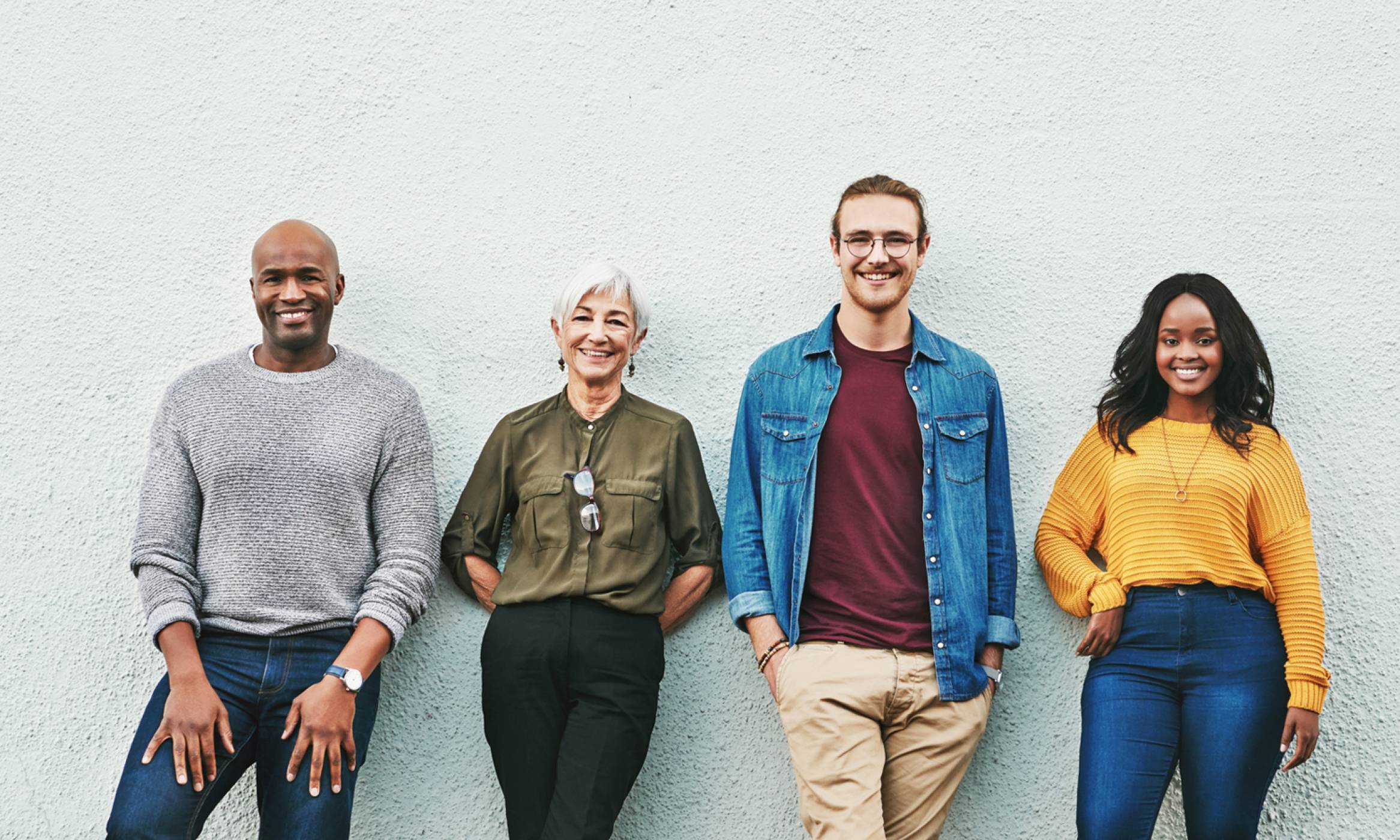 A multi-ethnic group of men and women of different hair types with thick and healthy hair happily pose for a picture with trees behind them.