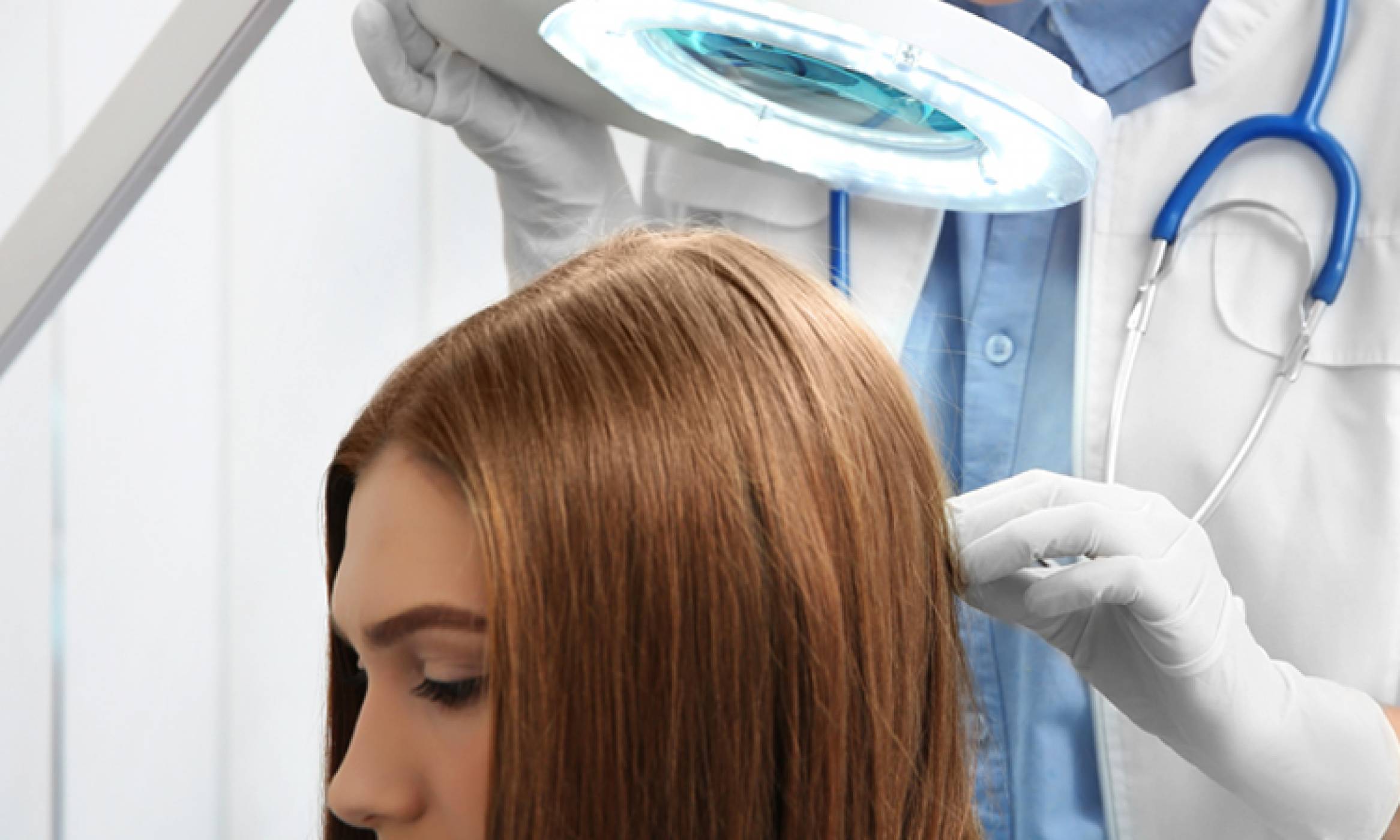 A female doctor is examining the scalp of a woman using a magnifier to treat hair thinning with a hair regrowth treatment.