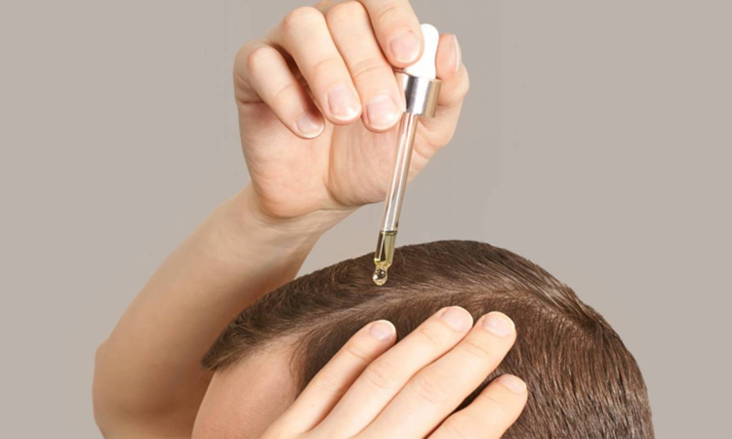 A confident man with a full head of hair is applying a hair regrowth product that treats hair loss.