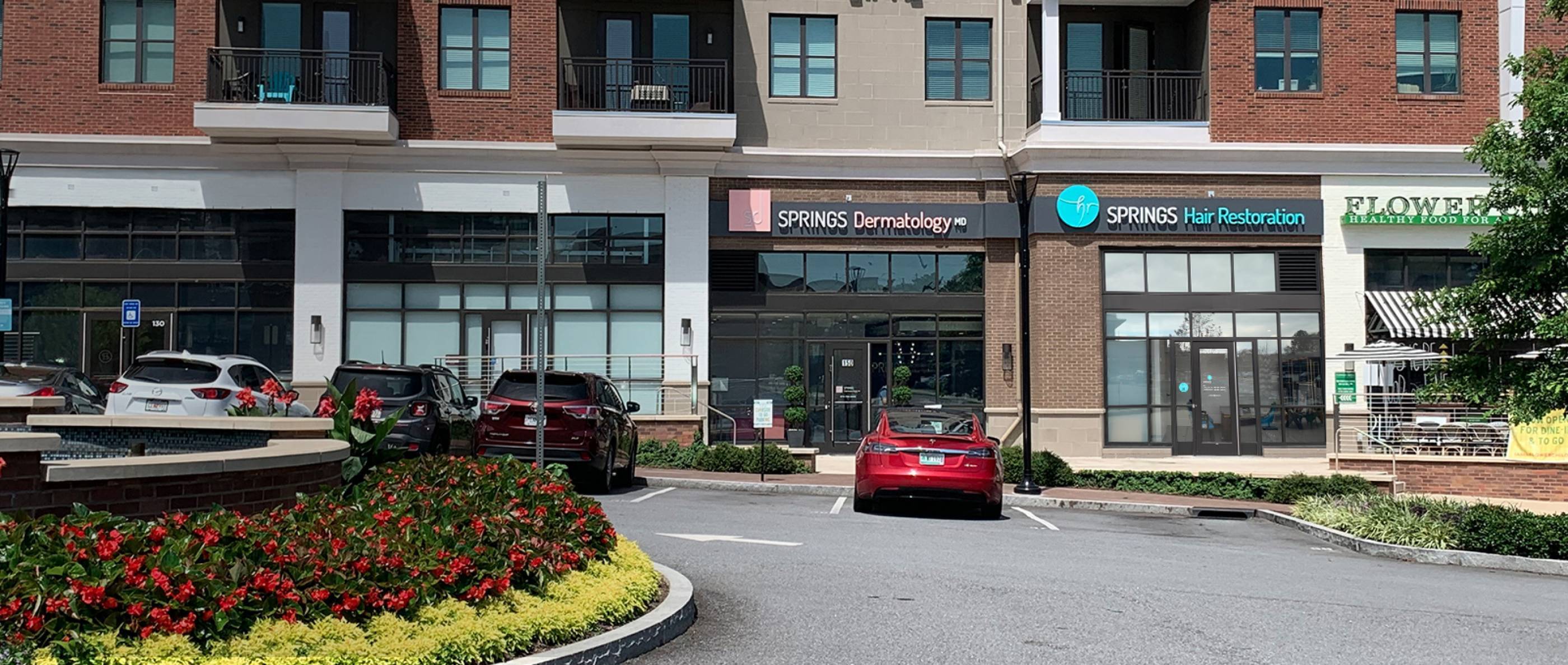Outdoor shot of the facade of the clinic, Springs Dermatology is to the left of Springs Hair Restoration, Flower Childcafe to its right.