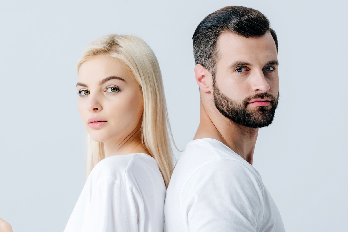 Image of a man and woman standing back to back, they are looking at us, they have some hair loss